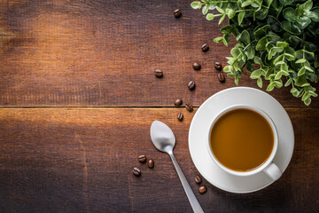 Top view of coffee in white cup with coffee beans And spoon with green trees on wooden background.