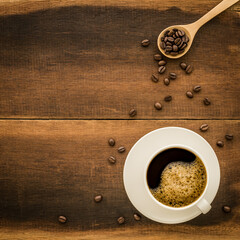 Top view of coffee in white cup And coffee beans with wooden spoon and copy space on wooden background.