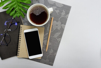 Desk top, view on desk with mobile phone, notebook, pencil, coffee, glasses, tree on gray background