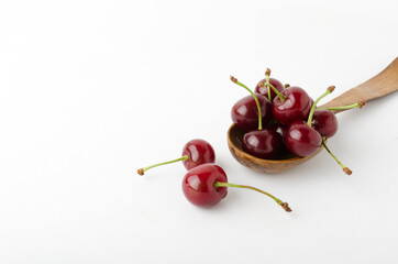Closeup of heap of cherries and wooden spoon on the white background
