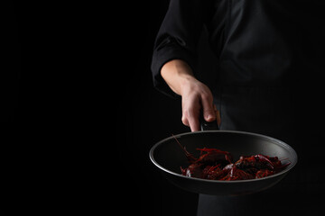Chef cook fries crayfish in a pan on a black background, menu