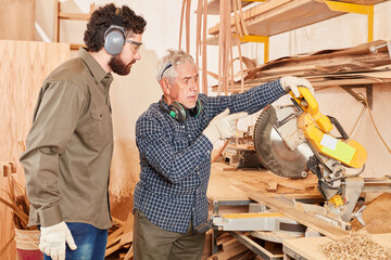 Carpenter master and apprentice at the chop saw