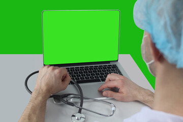 young man, doctor, pharmacist in a white mask is sitting at a laptop with a green screen, the concept of gadgets, modern technology in medicine, an empty form for video