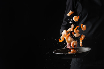 A professional chef cooks prawns by frying in a pan. Cooking seafood, healthy vegetarian food and...