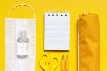 Stationery and medical mask on yellow background top view, copy space