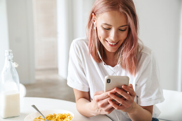 Photo of woman using cellphone and earphones while having breakfast