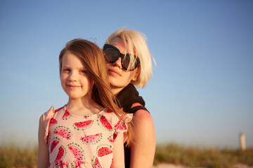 Smiling mother and beautiful daughter having fun on the beach. Portrait of happy woman giving a piggyback ride to cute little girl with copy space. Portrait of kid embracing her mom during summer.