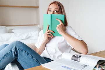 Image of shocked pretty woman reading book while doing homework