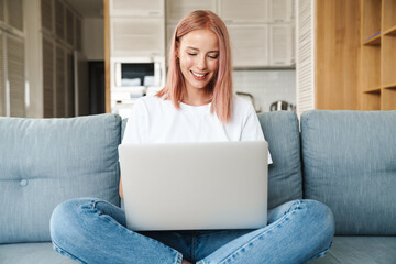 Image of woman working with laptop and smiling while sitting on sofa
