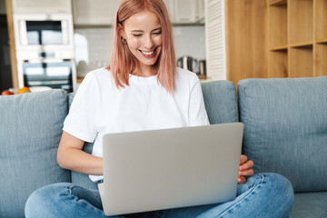 Fototapeta na wymiar Image of woman working with laptop and smiling while sitting on sofa