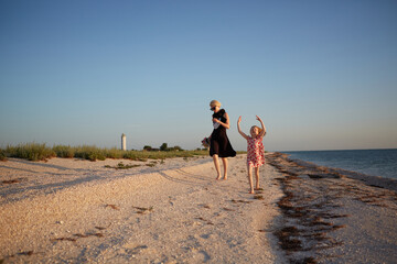 Smiling mother and beautiful daughter having fun on the beach. Portrait of happy woman giving a piggyback ride to cute little girl with copy space. Portrait of kid and her mom during summer