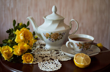 Still life and yellow roses, teapot with cup and round cookies on brown table