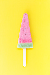 A woman's hand holds ice cream on a stick on a yellow background, copy of the space