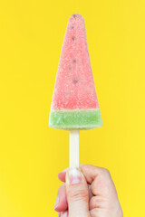 A woman's hand holds ice cream on a stick on a yellow background, copy of the space