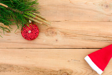 Obraz na płótnie Canvas Red Christmas ball, green pine branch with cones on a wooden background. The concept of new year and Christmas, warm knitted things, Santa Claus hat. Flatlay, top view. Space for text