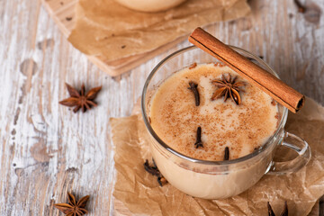 Glass cups of traditional Indian masala chai on light wooden background. Ingredients of beverage black tea, ginger, cinnamon, cardamom, anise stars