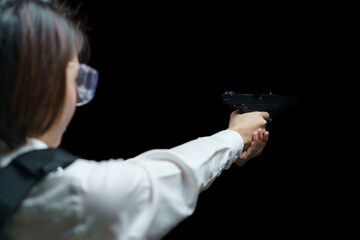 Woman wearing bulletproof vest shoots with gun at a target at indoor gun range.