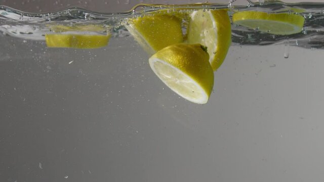 half of lemons and lemon slices dropped into the transparent aquarium with water on grey background Slow motion from 120 fps