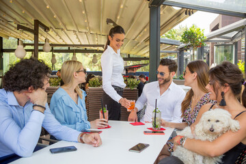 Naklejka premium Waitress serving drinks to a group of friends in the garden restaurant