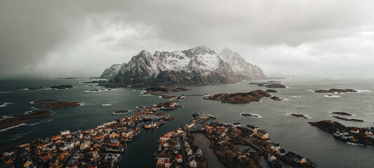 Henningsvær aerial panorama at winter. Small houses on islands, mountains covered with snow on horizon and spectacular sky. 