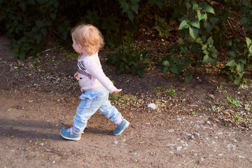A small baby girl walks on a stone road