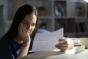 Worried woman reading letter at night at home