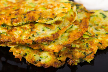 Fritters of courgettes with sour cream on black dish