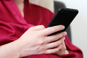 Woman using smartphone at home in a bed, girl in red lace nightie with mobile phone. Concept of online addiction, sms, social media