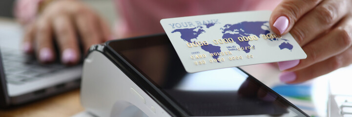 Girl at table holds credit card over bank terminal. Bank employee female offers to install wireless...