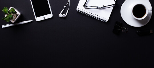 On a black background is a white notebook, pen, headphones, a cup of coffee, a phone, glasses. Top...