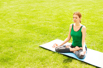 A woman practices yoga outdoors on the grass. Copy space