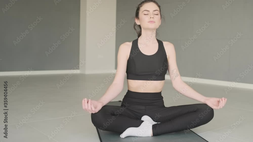 Sticker A calm woman is meditating while sitting on yoga mat in studio