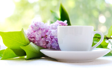 white coffee Cup with a branch of lilac on the background of young greenery. The concept of tenderness and celebration of Valentine's day, mother's day or women's day