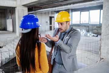 Frustrated architect talking to his female colleague and he is angry because construction works did...