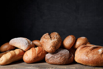 Variety of loaves of bread and buns on wooden table background.
