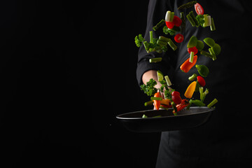 Professional chef fry vegetables in a pan, freeze in motion, on a black background, banner, veggie food, tasty and wholesome food