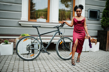 Portrait of a beautiful natural young African woman with afro hair. Black model in red silk dress with mountain bike.