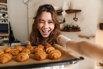 Cheerful young girl taking a selfie and showing baked cookies