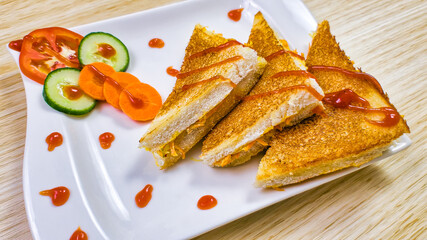 Crispy toasted Vegetable sandwiches garnished with Ketchup along with sliced vegetables.