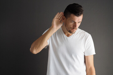 Man in white t-shirt hearing something over gray background.