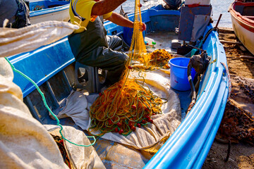 Fototapeta na wymiar Fisherman is empty fish from net in his small boat