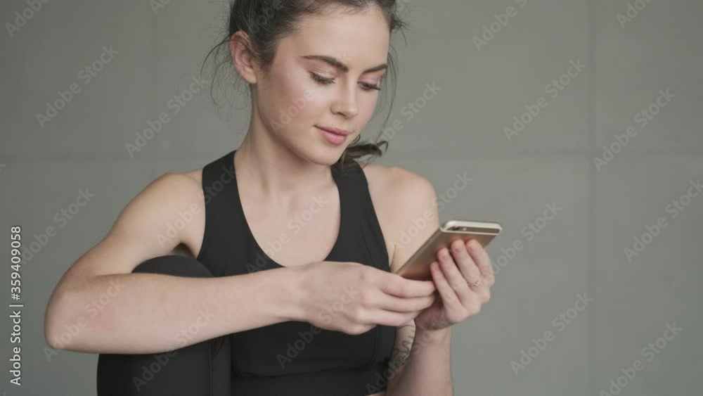 Poster a close-up view of a pretty nice young woman in a black tracksuit is using her smartphone before tra