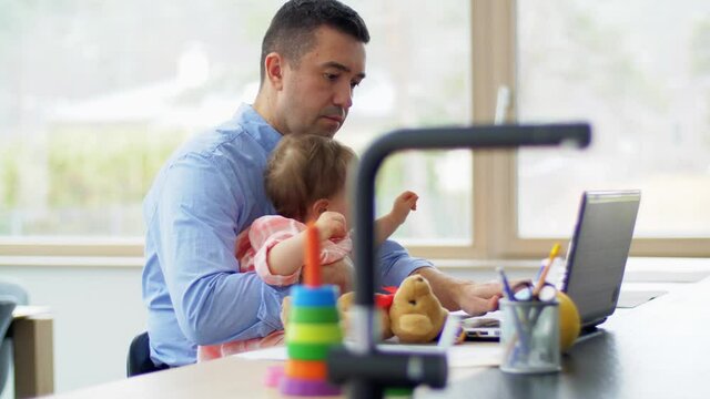 remote job, multi-tasking and family concept - middle-aged father with baby working on laptop at home office