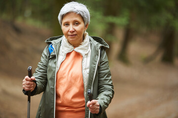 Waist up portrait of active senior woman looking at camera while enjoying Nordic walk during hike...