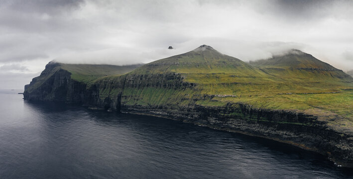 Cliff edge above ocean aerial panorama shoot on Faroe Islands. Overcast sky and green mountains.