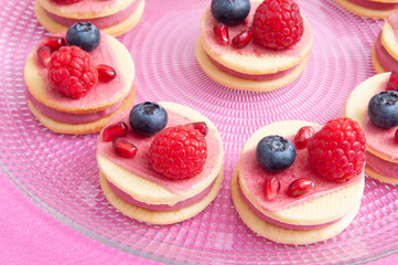 sandwich cookies with pink cream and fruit on pink background, transparent plate