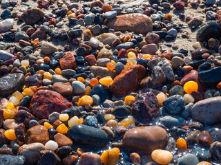 Small amber stone and pebbles on the sandy beach. Shallow wet amber washed by waves. Natural mineral at the Baltic sea coast.  Short focus.