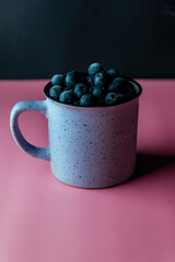 vertical composition fresh blueberries in a blue cup on a pink background. with the place for copy space.