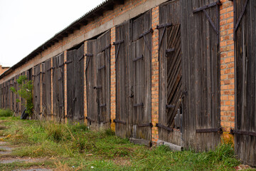 Old cowshed. Large wooden gate and dried wood. Old brick building