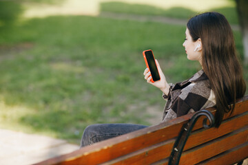 Young girl using mobile smart phone in the park. Internet, using smartphone, fashion model, post in instagram, facebook concept